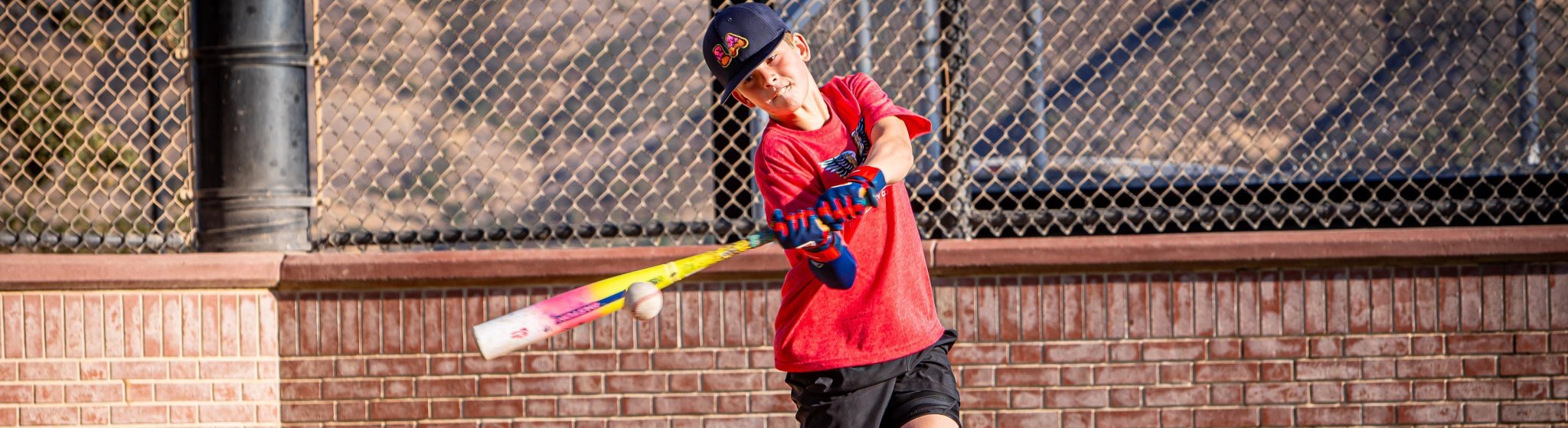 Child in red shirt and black shorts holding a baseball bat.